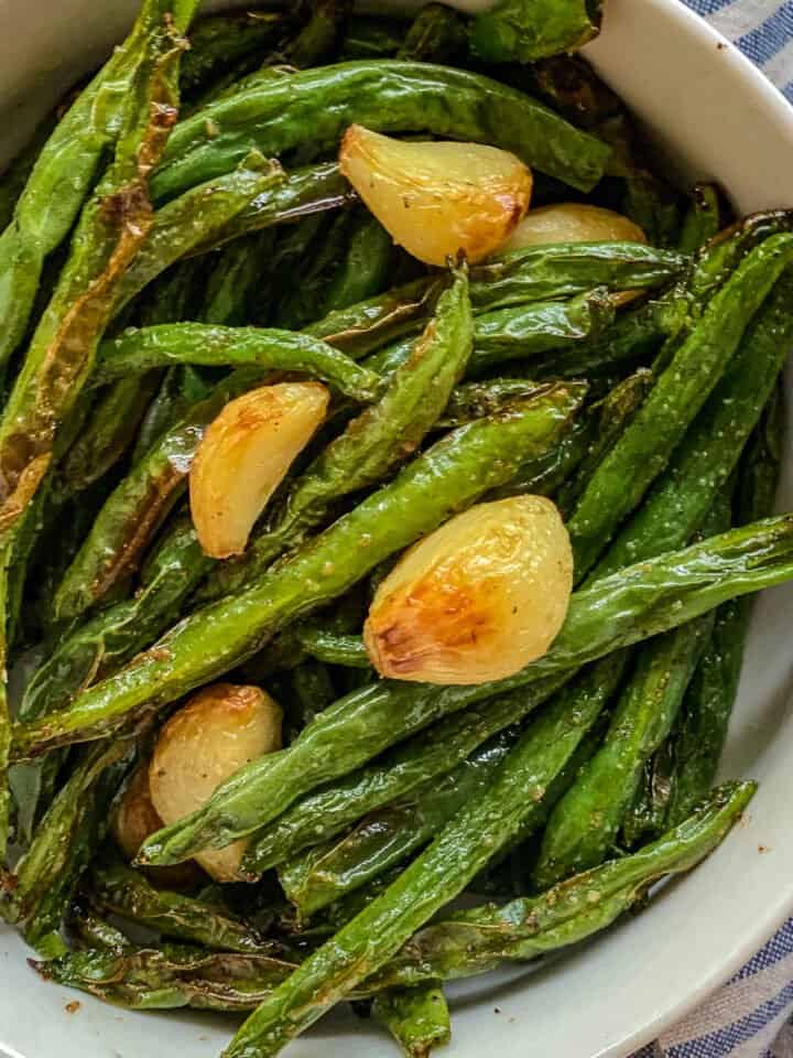 White bowl of green beans with garlic divided up close.