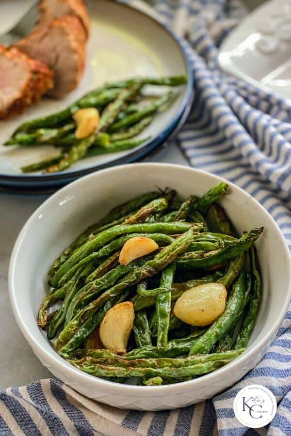 White bowl of green beans with garlic on top of a blue and white stripped napkin cloth