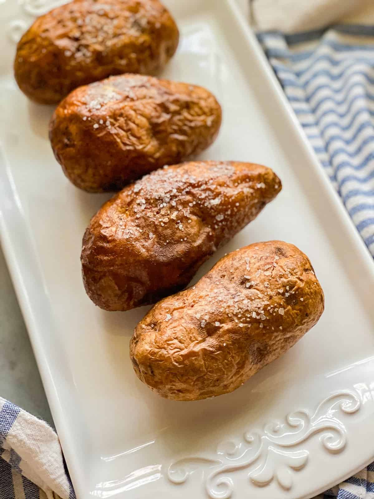 a white rectangular plate with four bakes potatoes with salt.