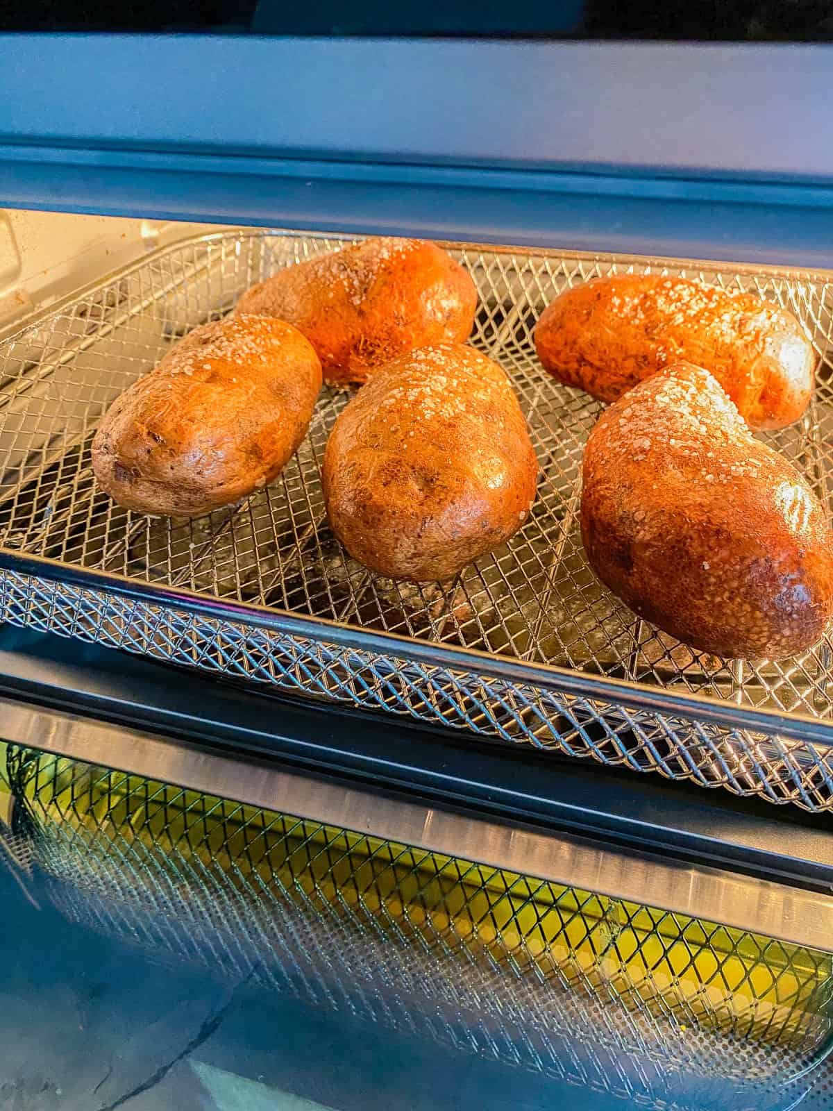 five uncooked potatoes on a silver rack in a oven.