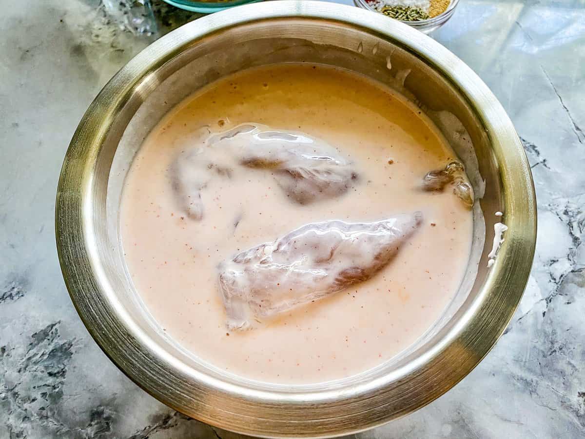 a silver bowl with pink sauce with two pieces of uncooked tenders inside.