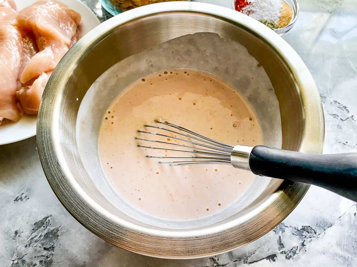 silver bowl with pink sauce and a silver whisk.