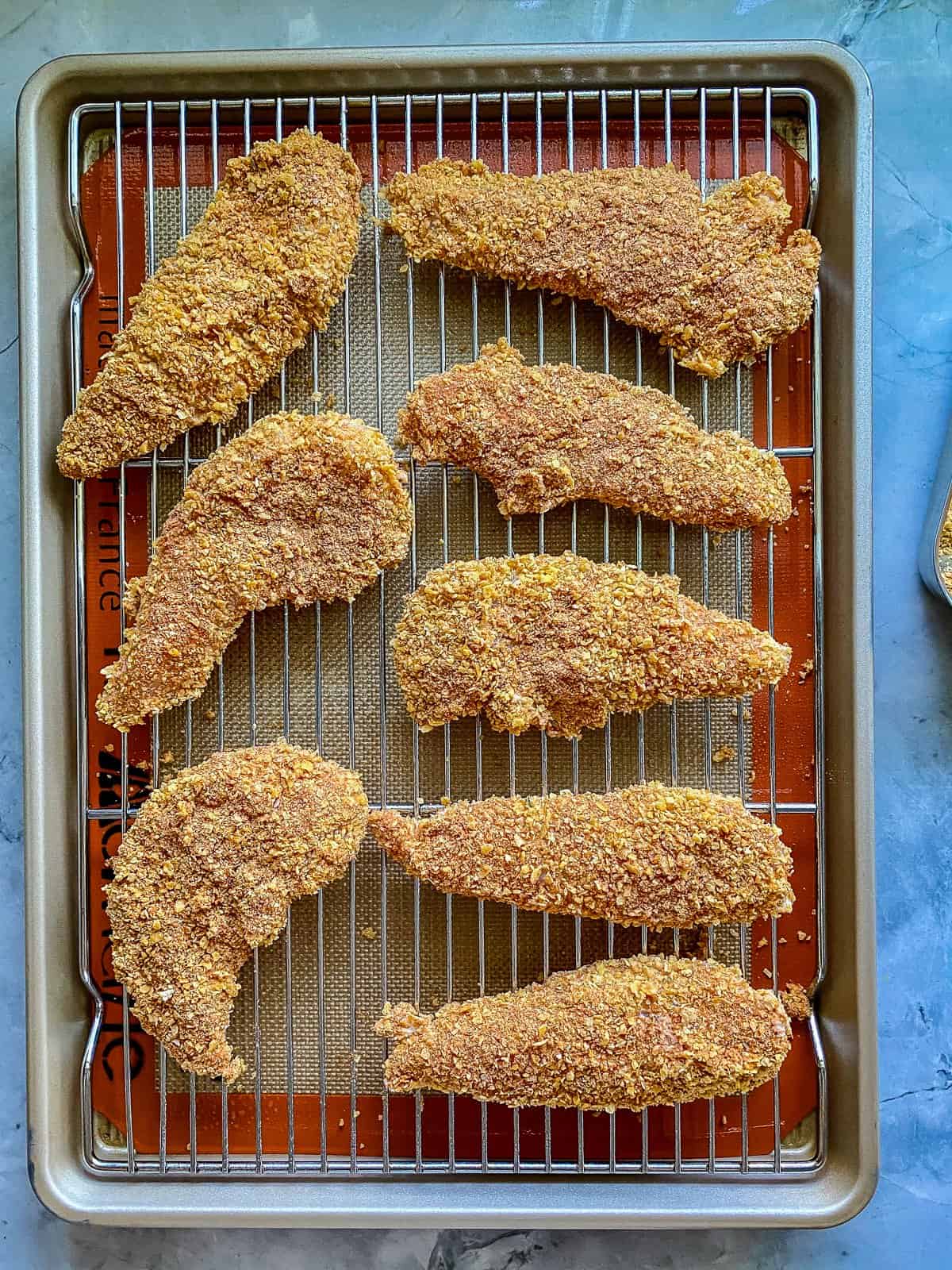 silver pan with red trim eight chicken tenders covered in golden brown corn flakes.