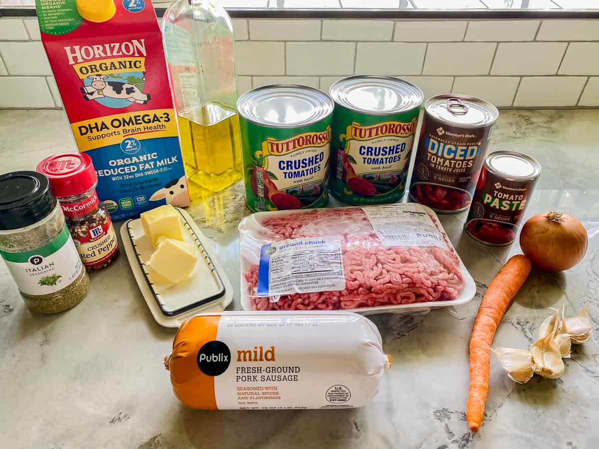 Seasonings, milk, olive oil, butter, and meat on a white marble counter.