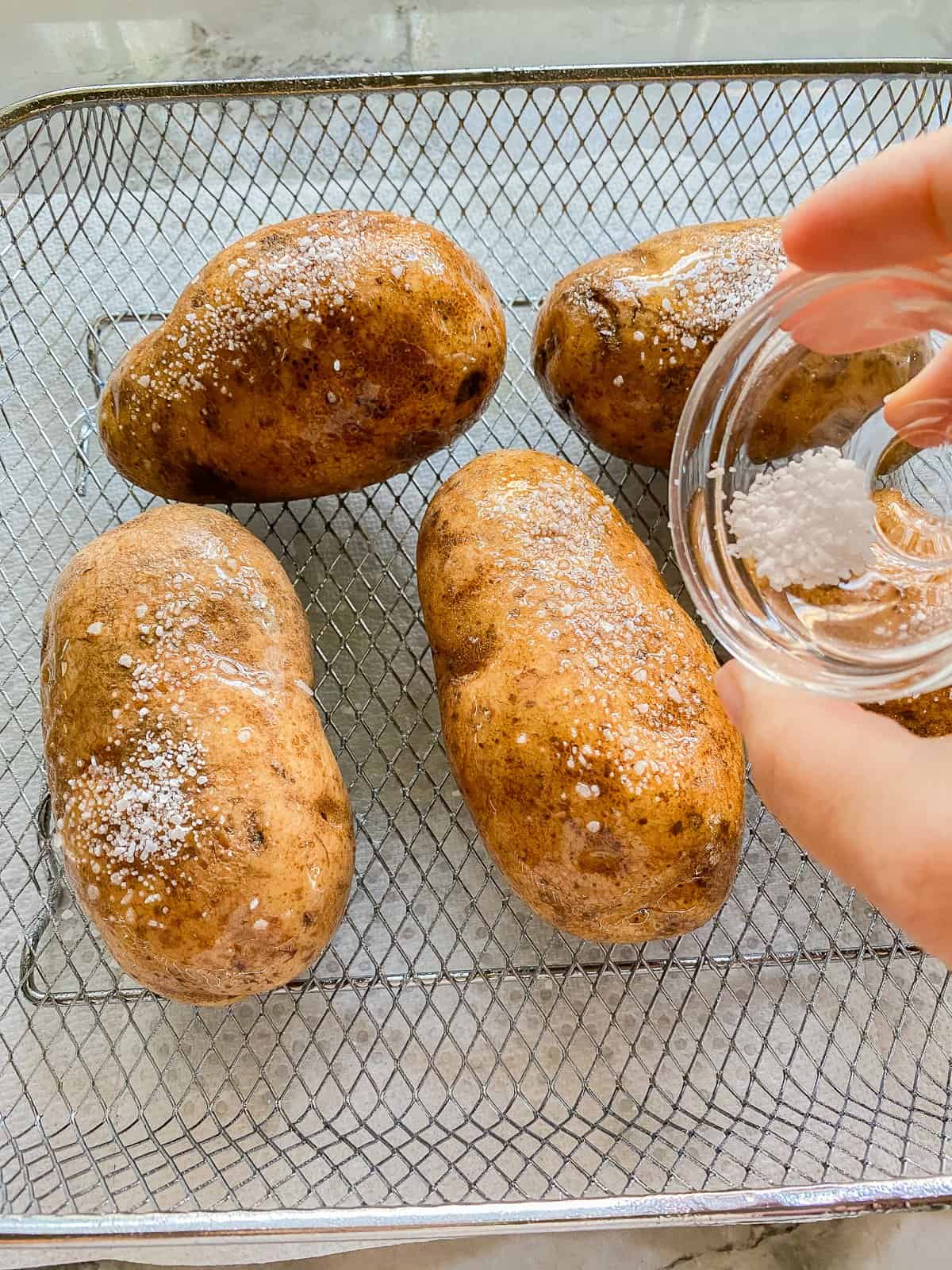 five whole potatoes with salt on top of a white marble counter.