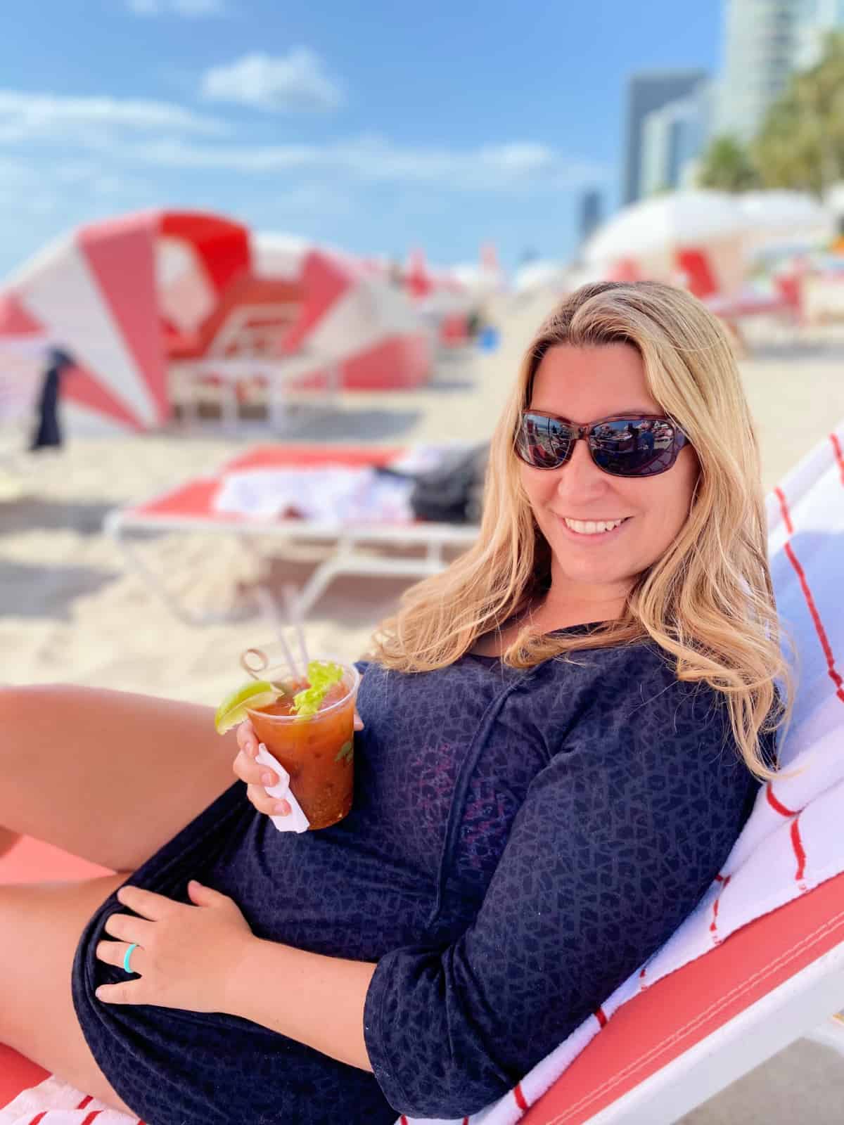 Female laying on a beach chair holding a bloody mary.