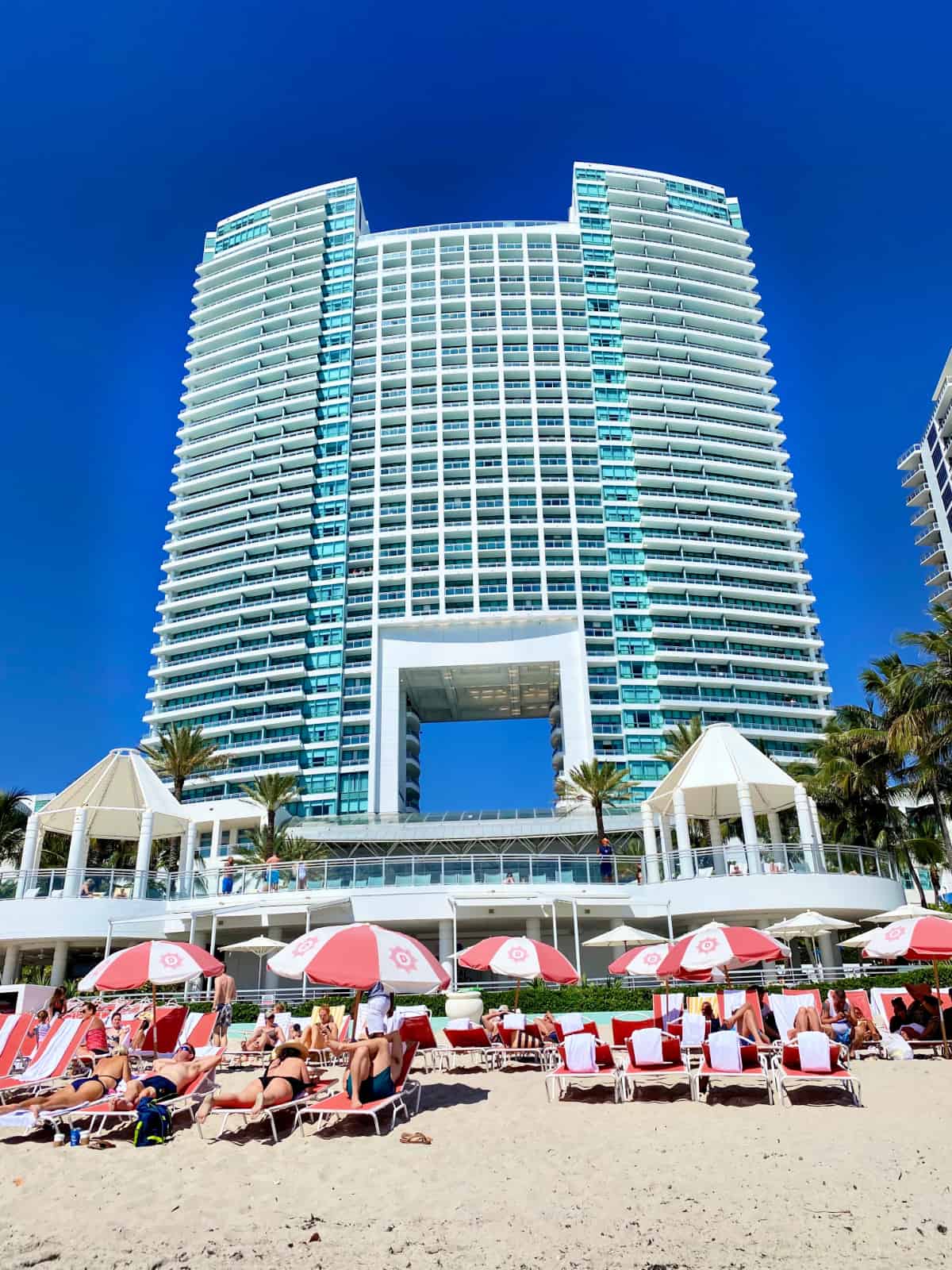 Tall building on the beach with lounge chairs and beach goers in front. 