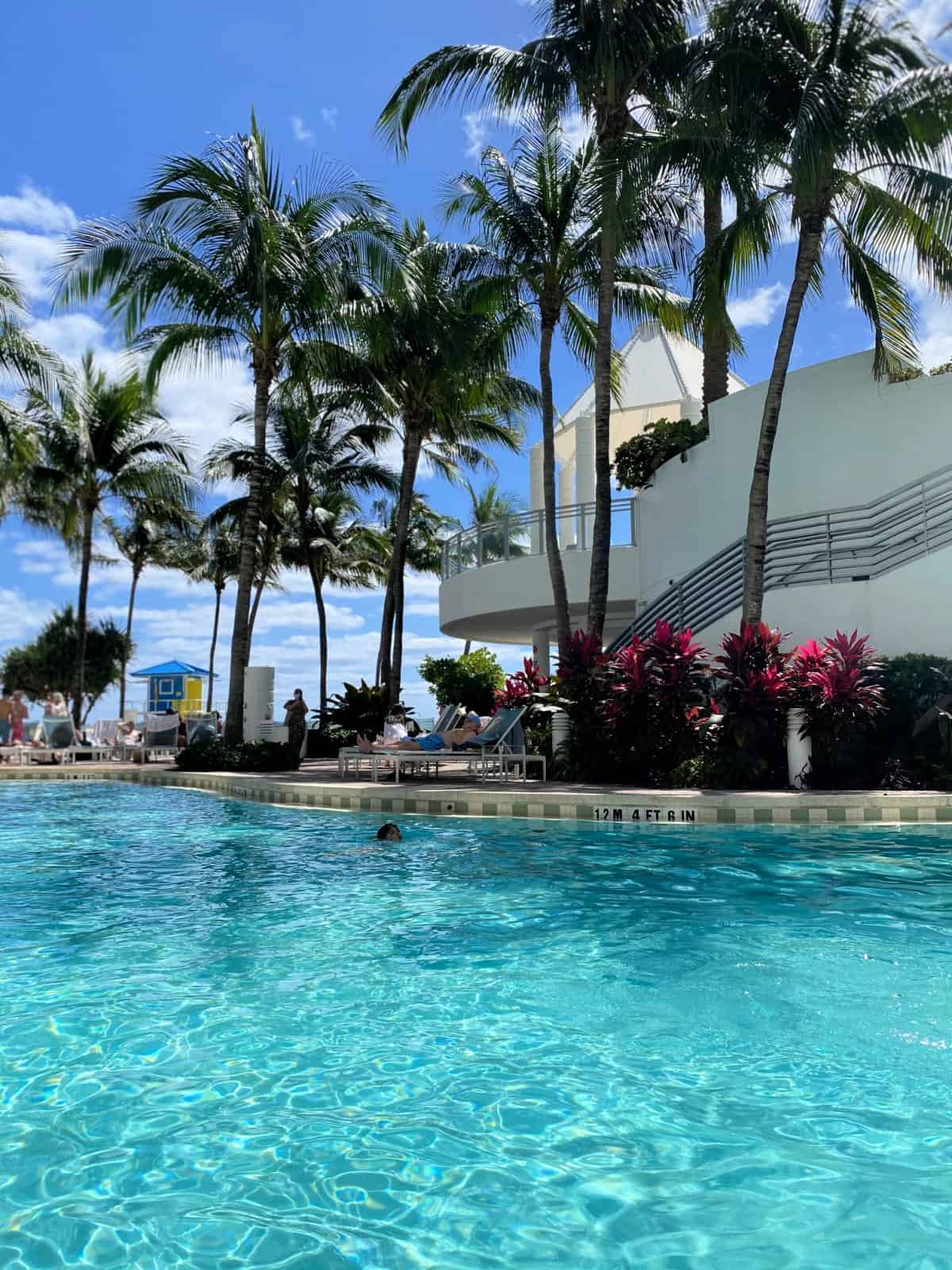 Bright blue pool with palm trees next to it.