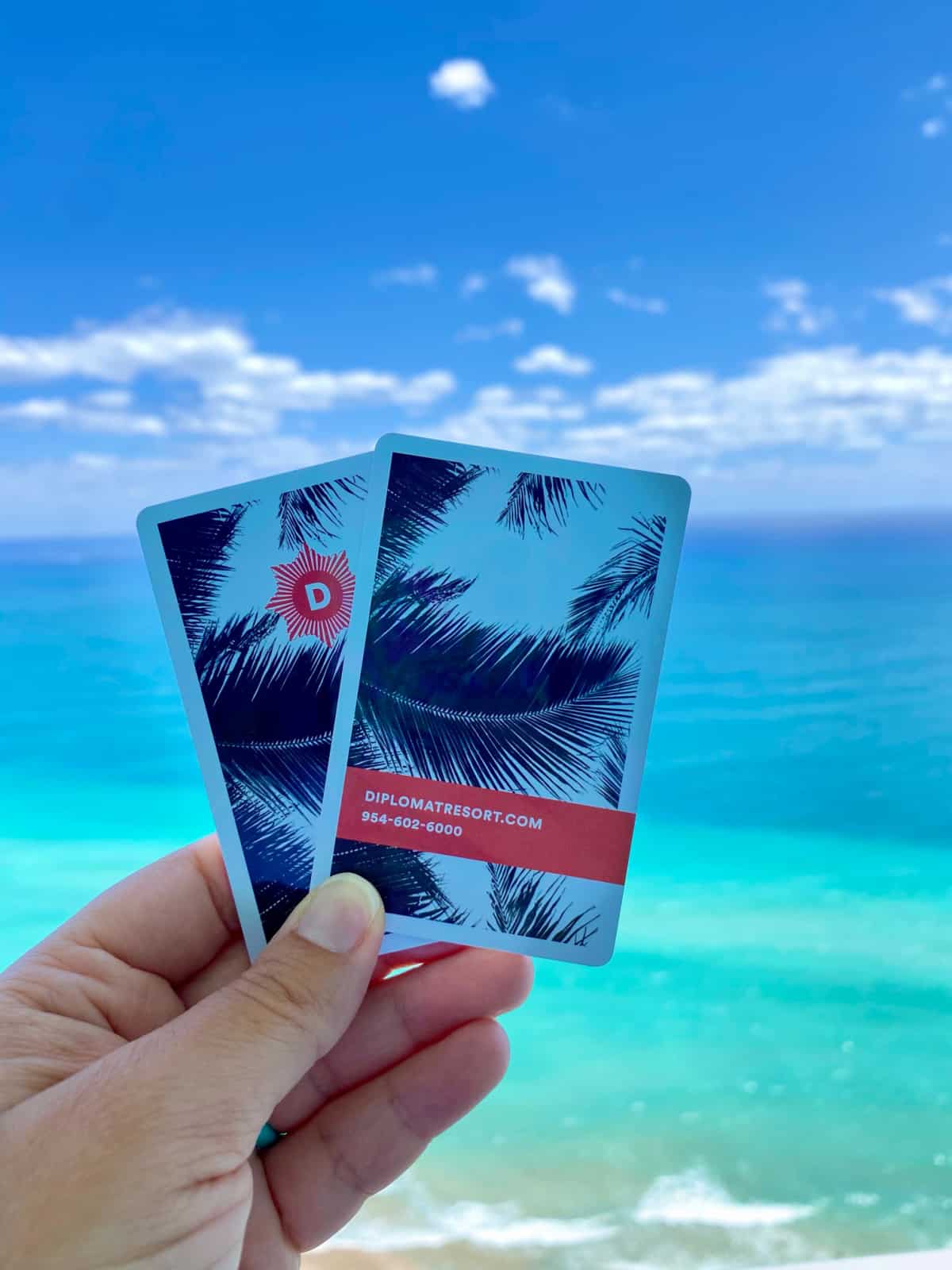 hand holding two room cards with the ocean in the background.