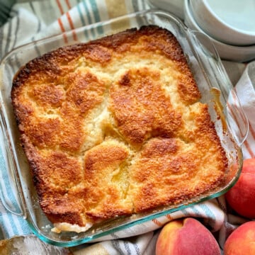 Glass baking dish filled with peach cobbler resting on a striped dish cloth.