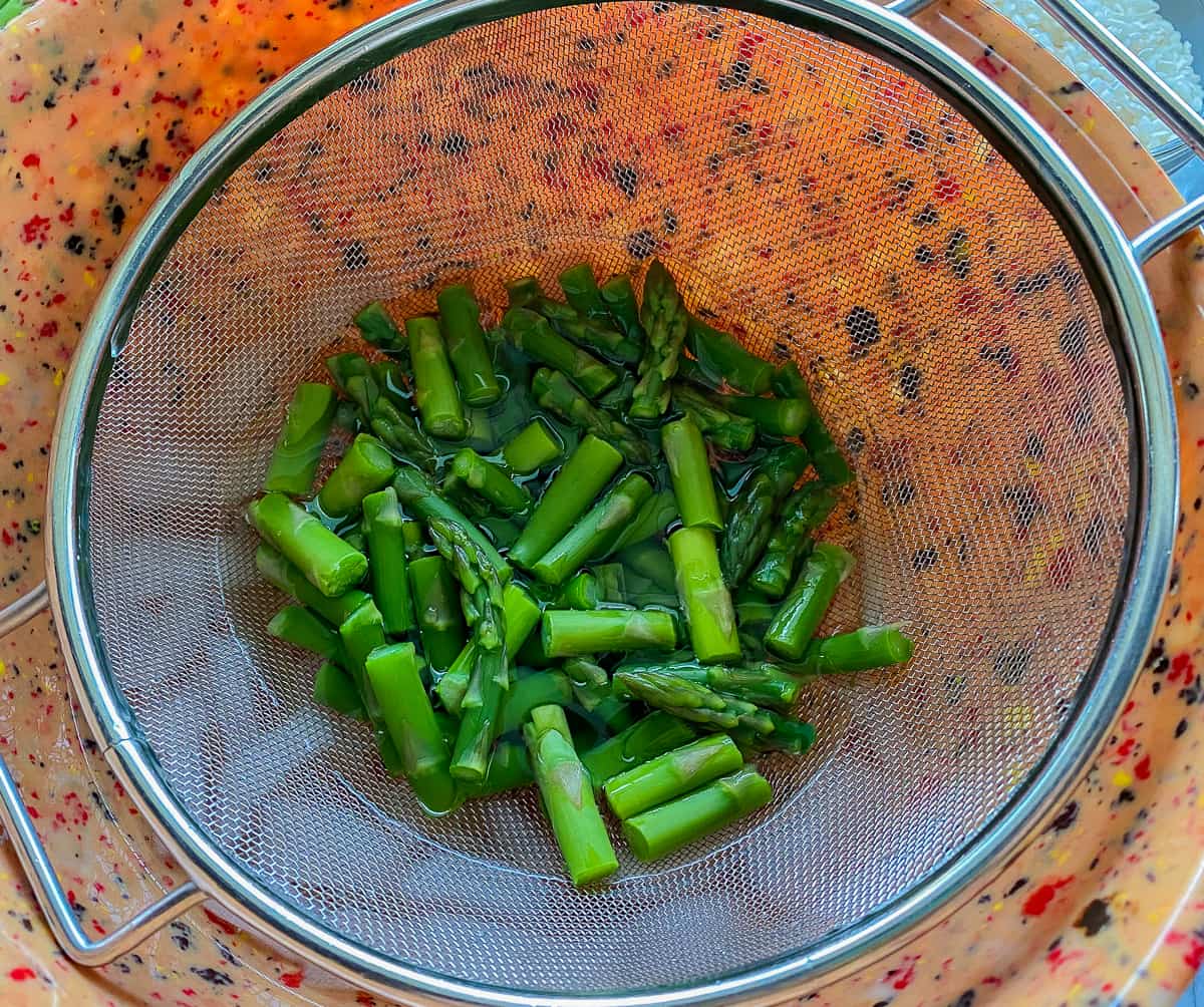Chopped blanched asparagus in a mesh collander.