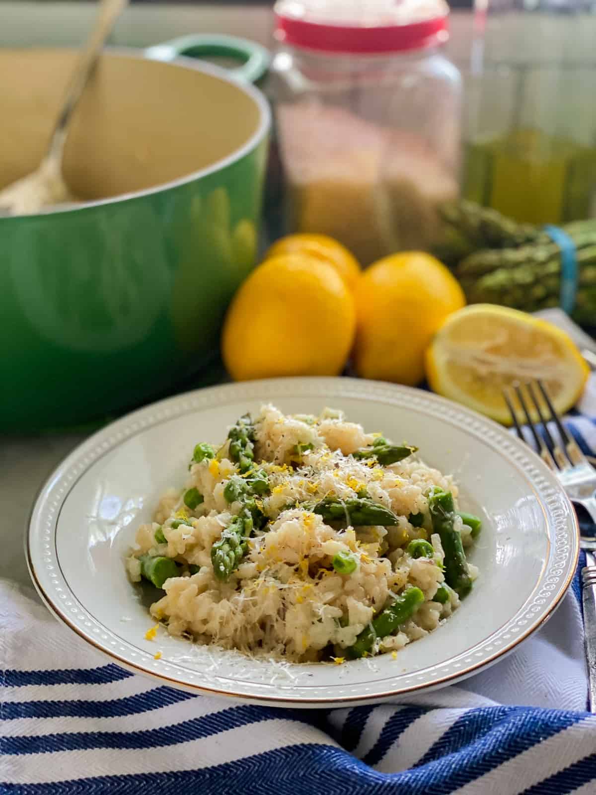 White bowl with risotto, asparagus, peas, lemon zest, and cheese.