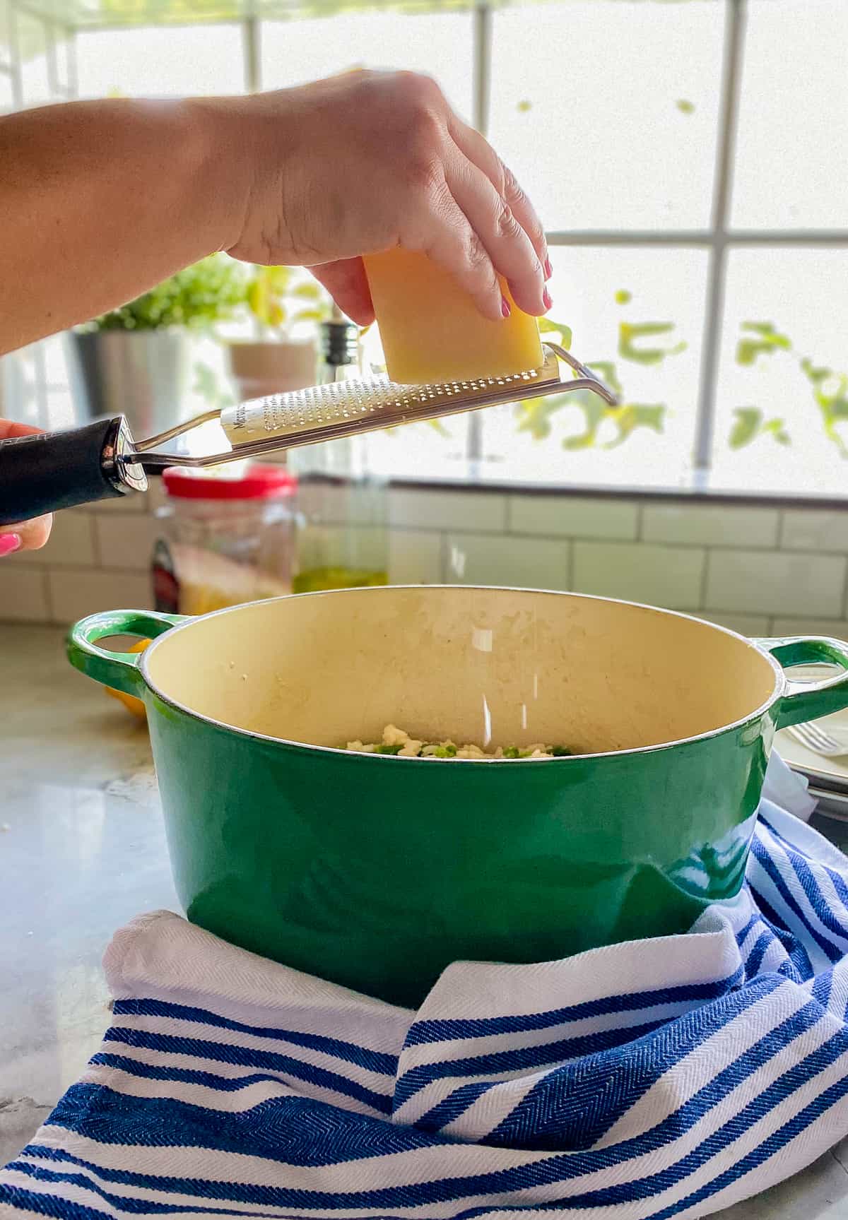 Hand grating block of cheese over a green pot.