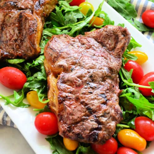 grilled steak on a bed of arugula and tomatoes on a white platter.