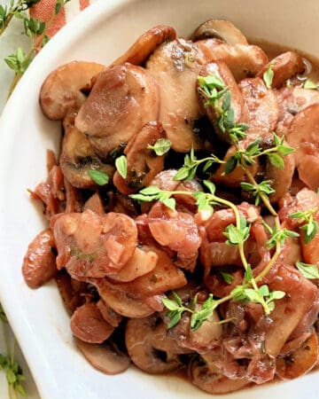 White dish filled with mushrooms and onions with fresh thyme sprigs.