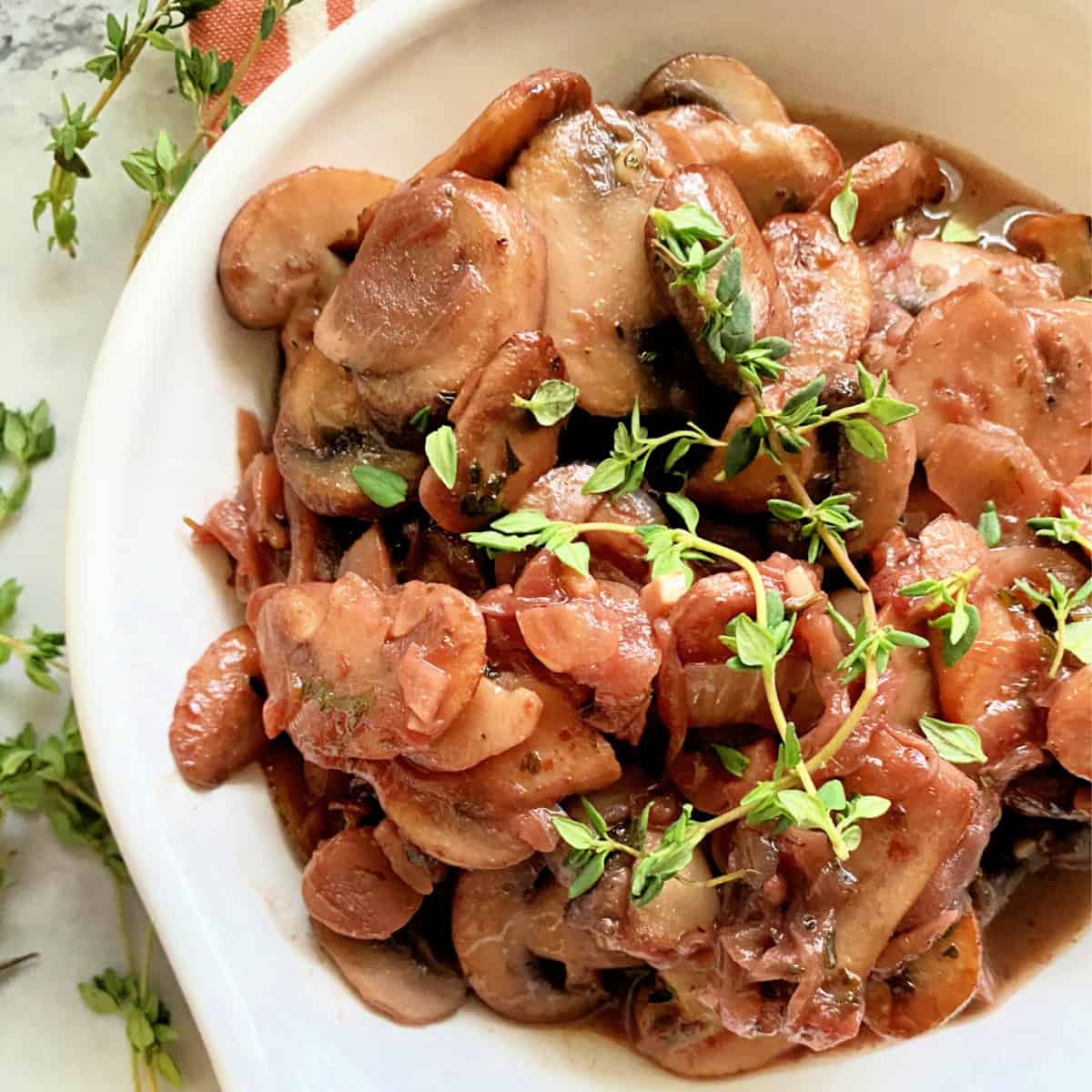 White dish filled with mushrooms and onions with fresh thyme sprigs.