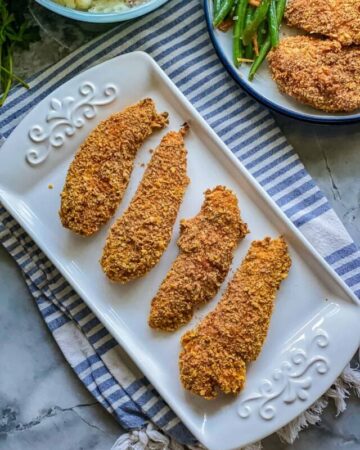 Rectangular white plate with four chicken tenders, with a second plate on top with green beans.