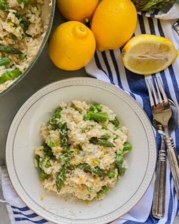 White bowl filled with risotto, asparagus, cheese, and lemon.