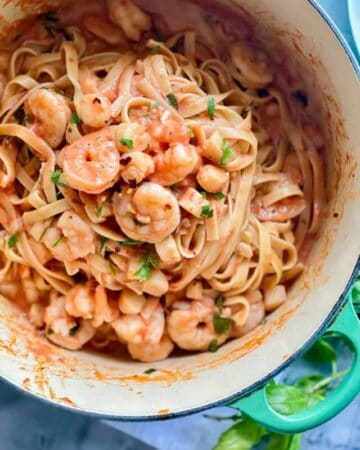 Pot with a teal green handle with noodles and red sauce, with shrimp and scallops inside of pot.