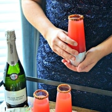Female in blue dress holding a champagne flute with pink juice.