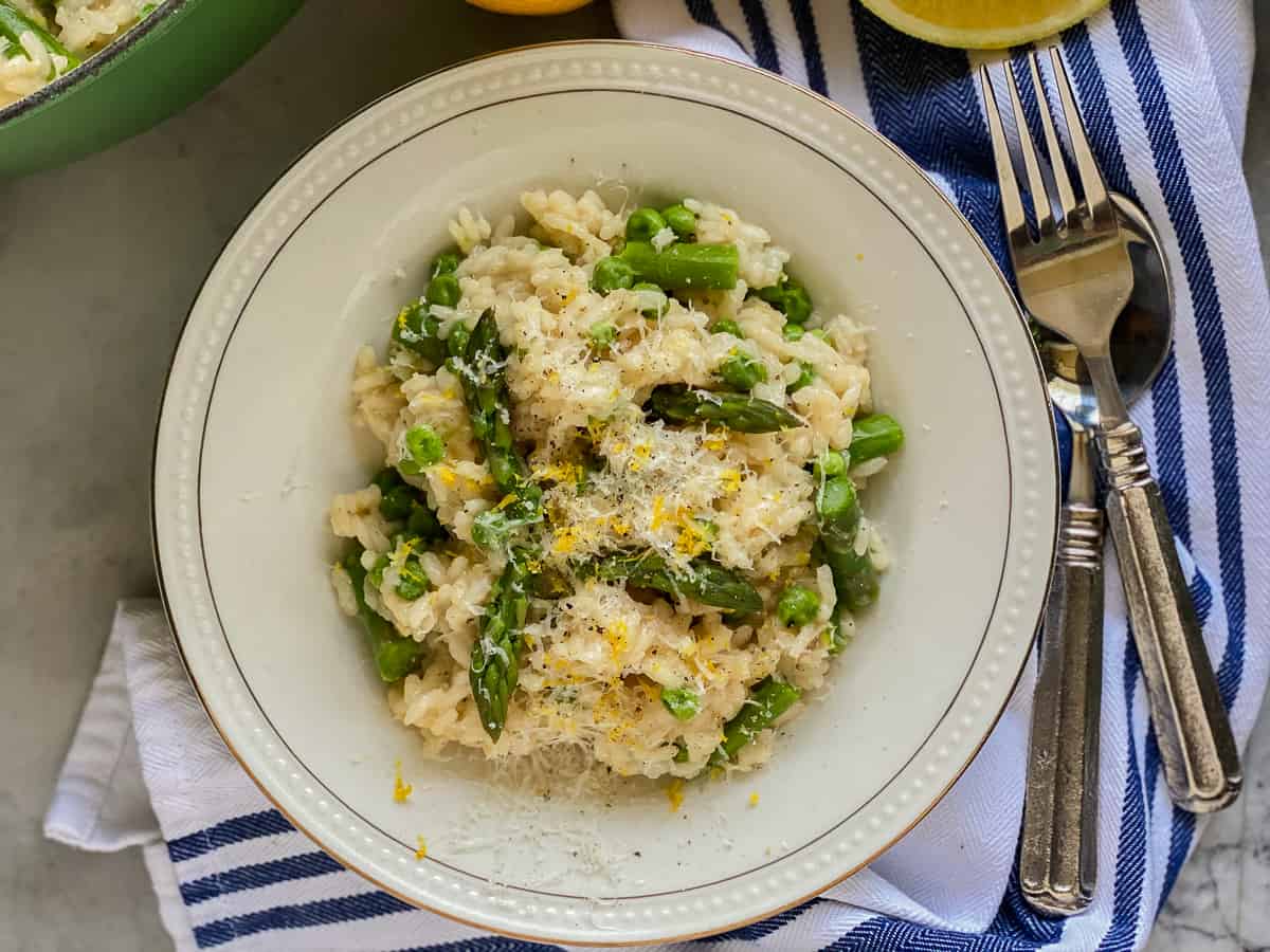White bowl filled with risotto, asparagus, peas, Parmesan cheese, and lemon zest. 