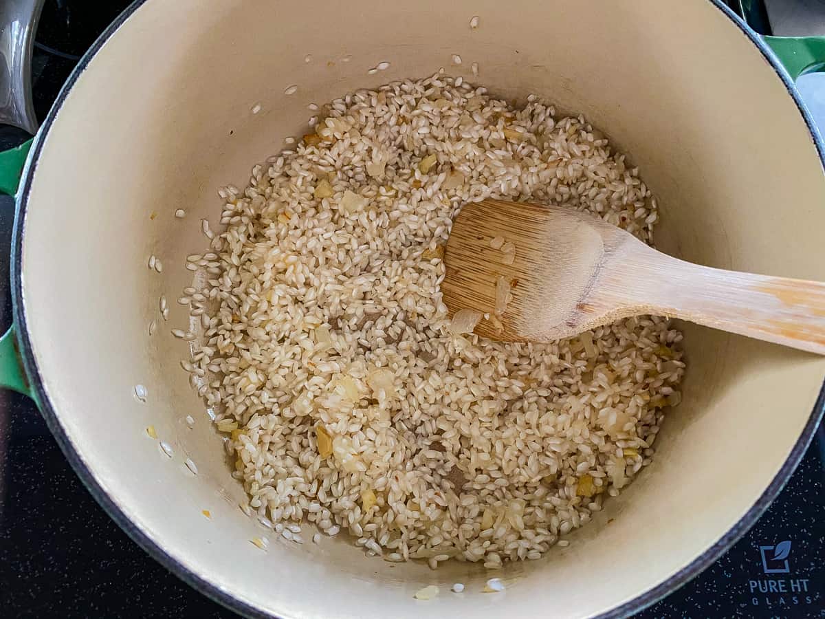 White pot filled with arborio raw rice with a wooden spoon.