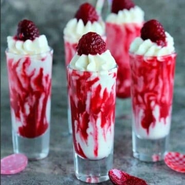 5 shot glasses filled with cream and raspberries.