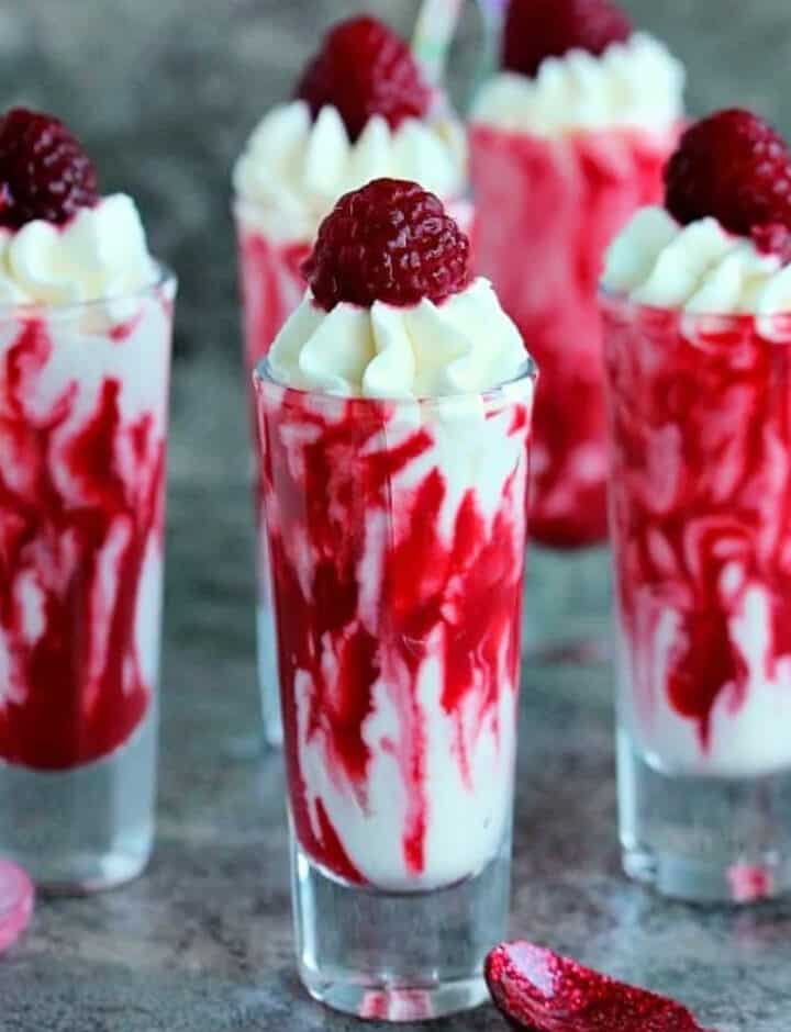 5 shot glasses filled with cream and raspberries.