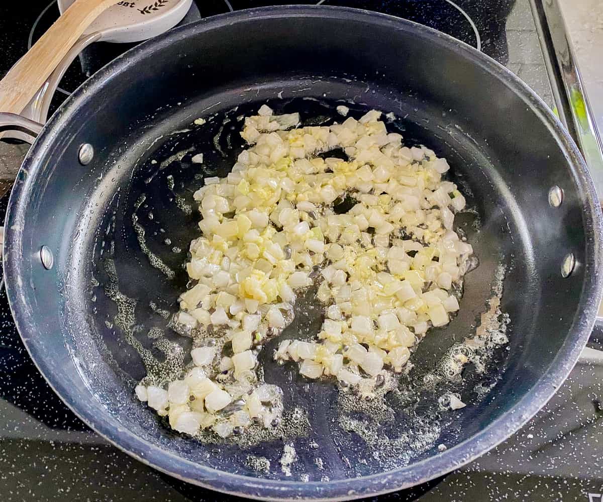 Black pan with white onions cooking on stove.