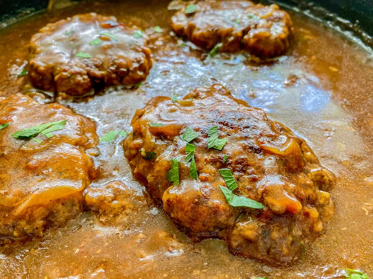 close up photo of four beef steaks with brown gravy with green onions on top as garnish.