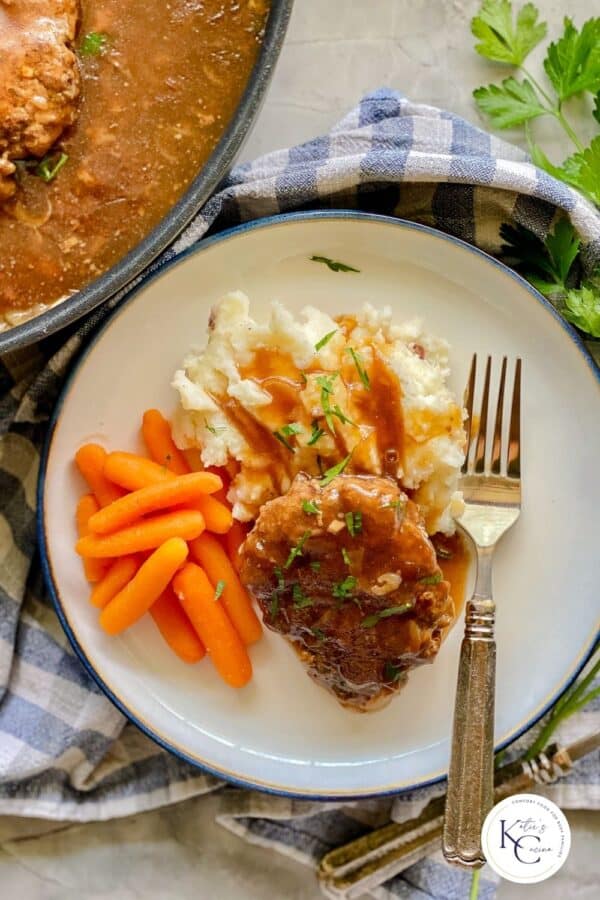 white plate with blue trim with white mash potatoes, orange carrots, brown steak with gravy with silver fork.