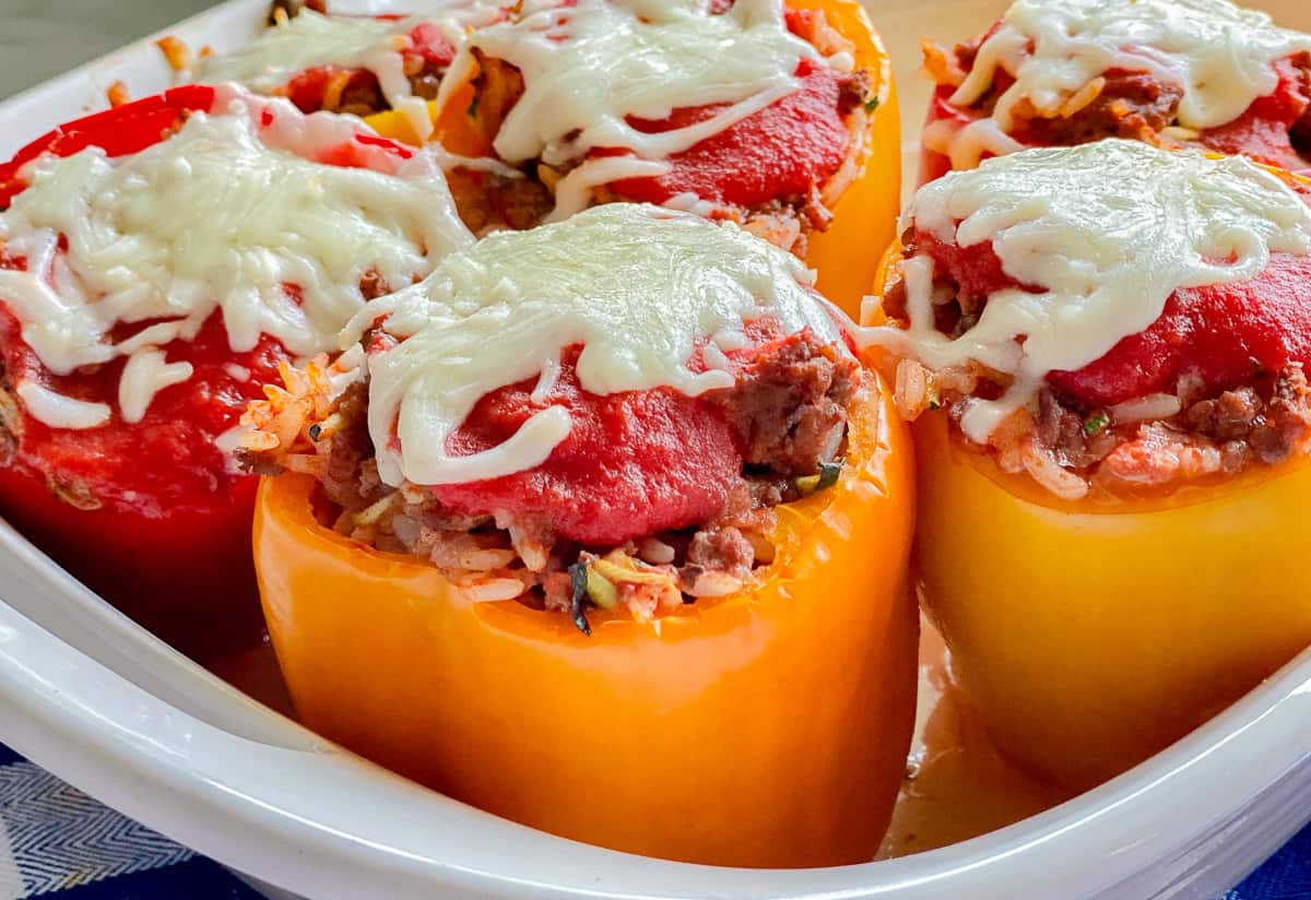 a white plate with four stuffed bell peppers with beef and rice with red sauce and melted white cheese on top.