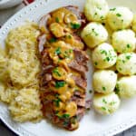 White platter with saurkraut, pork roast, and potato dumplings.