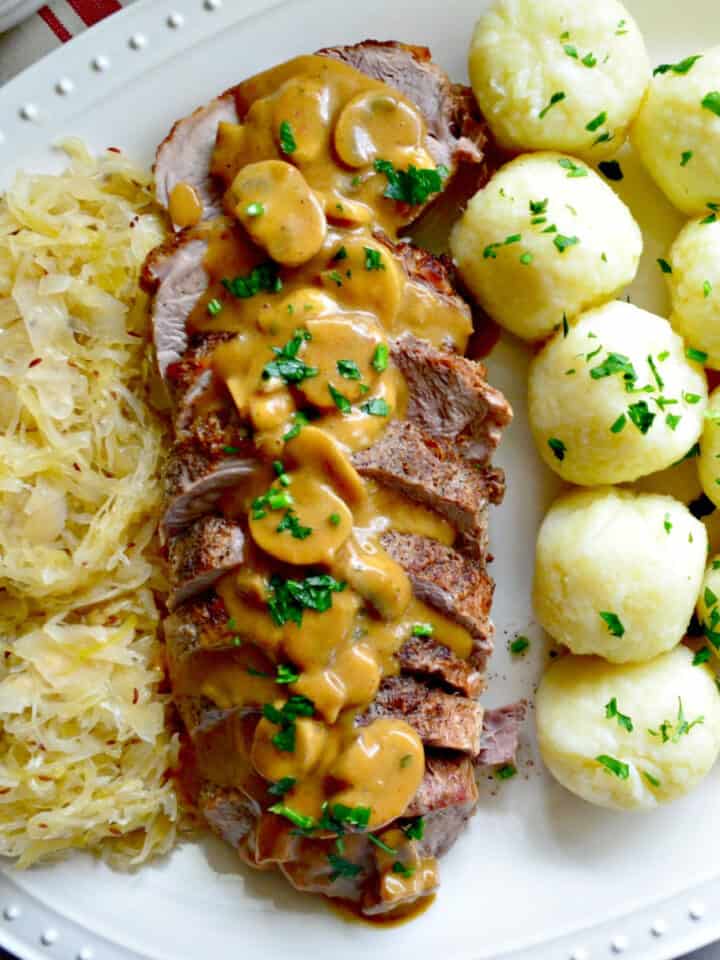 White platter with saurkraut, pork roast, and potato dumplings.