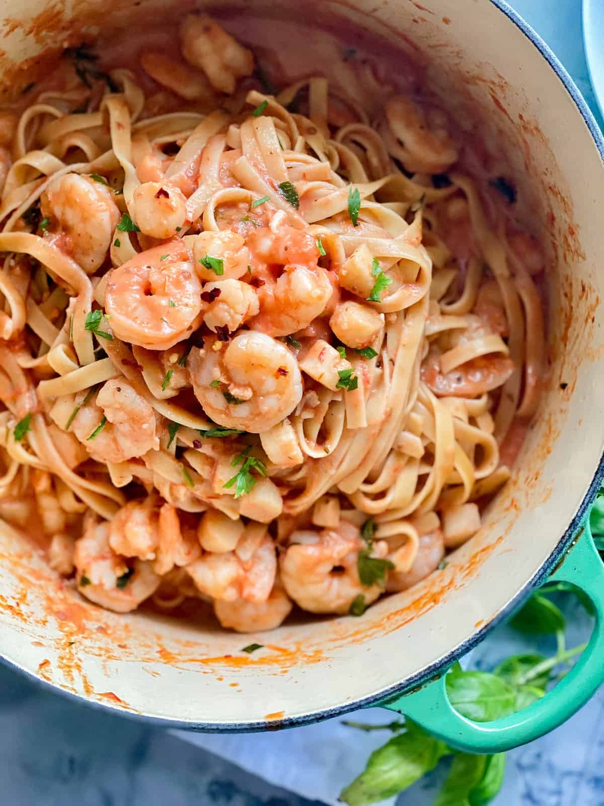 Pot with a teal green handle with noodles and red sauce, with shrimp and scallops inside of pot.