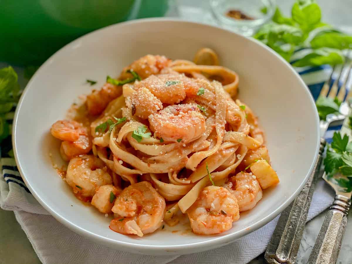 White plate with noodles with red sauce and shrimp and scallops.