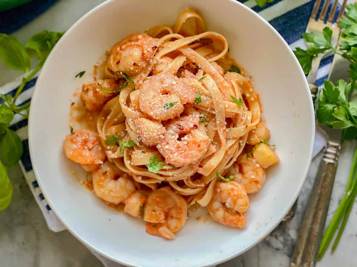 white glass plate with pasta noodles mixed in light red sauce with shrimps and scallop pieces and green parsley on top.