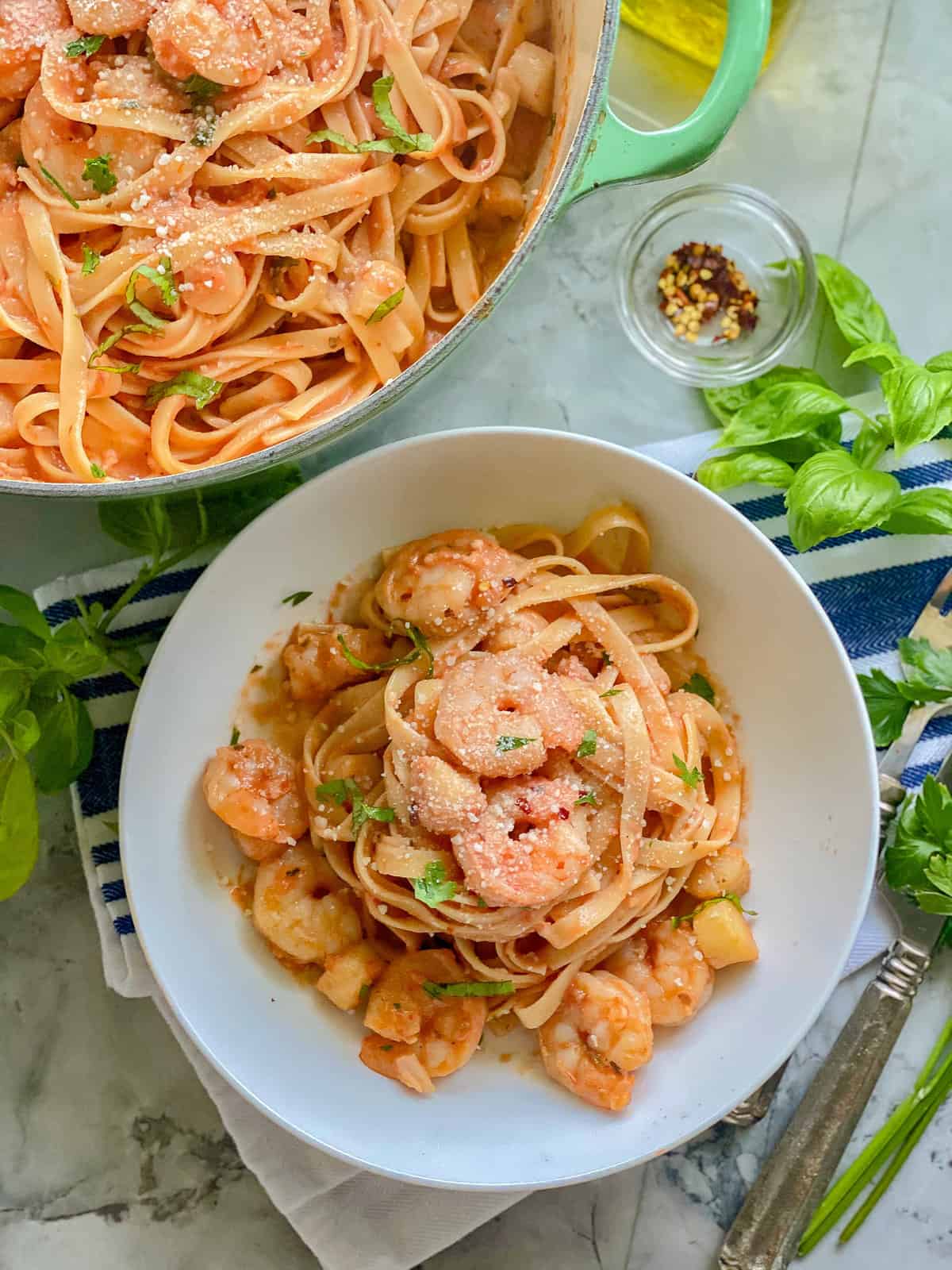 White plate with noodles with red sauce and shrimp and scallops.