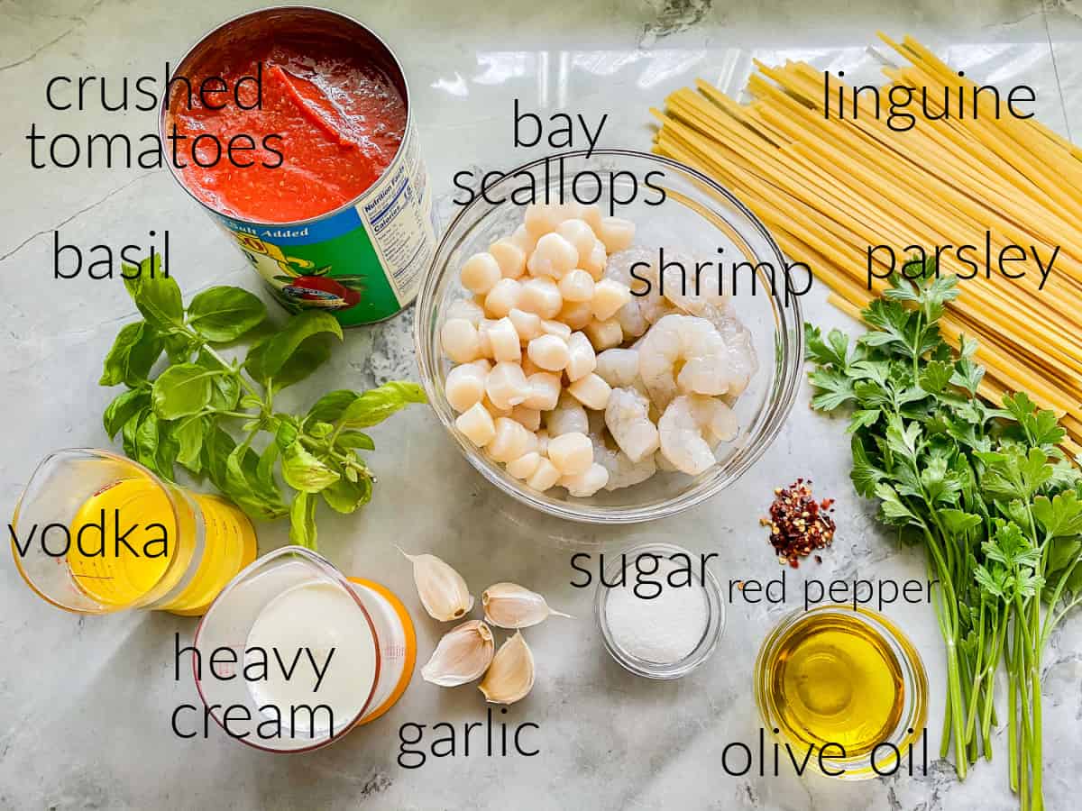 Ingredients on counter; crushed tomatoes, bay scallops, shrimp, parsley, linguine, basil, vodka, and heavy cream.