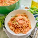 White bowl filled with pasta, shrimp, and scallops with a green pot in the background.