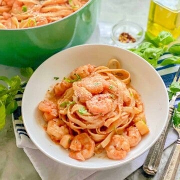 White bowl filled with pasta, shrimp, and scallops with a green pot in the background.