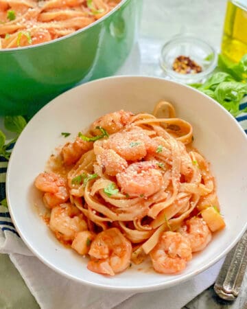 White bowl filled with pasta, shrimp, and scallops with a green pot in the background.