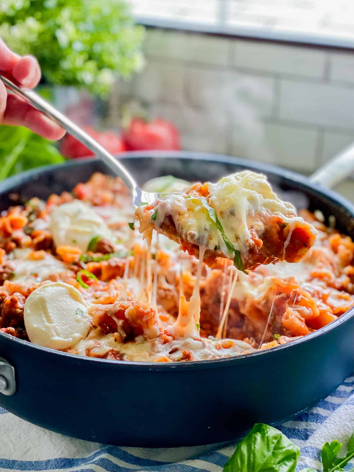 Black plate with lasagna with red sauce and green basil and on silver spoon.