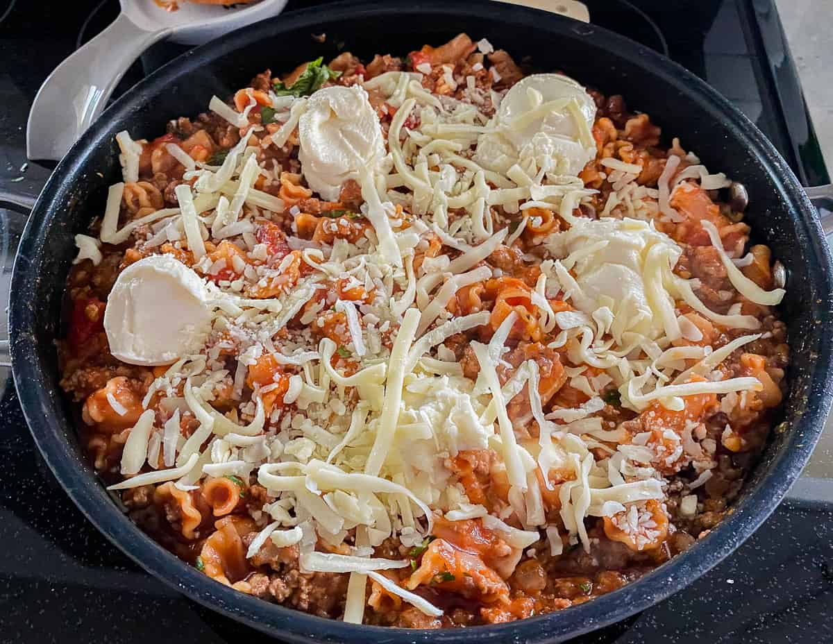 Black skillet with pasta and meat sauce with cheese on top.