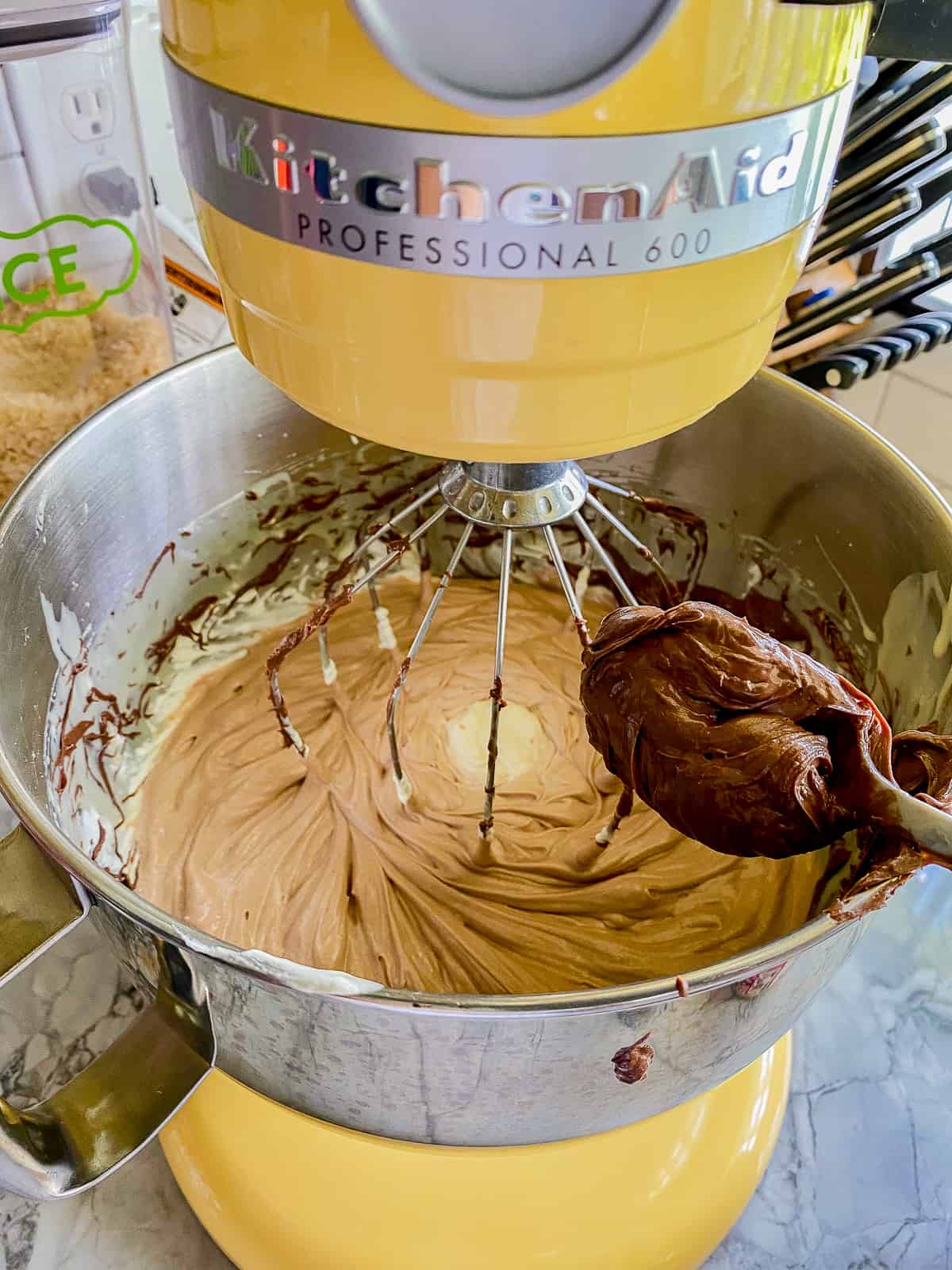 Yellow KitchenAid stand mixer with a balloon whisk and a spoon of chocolate nutella.