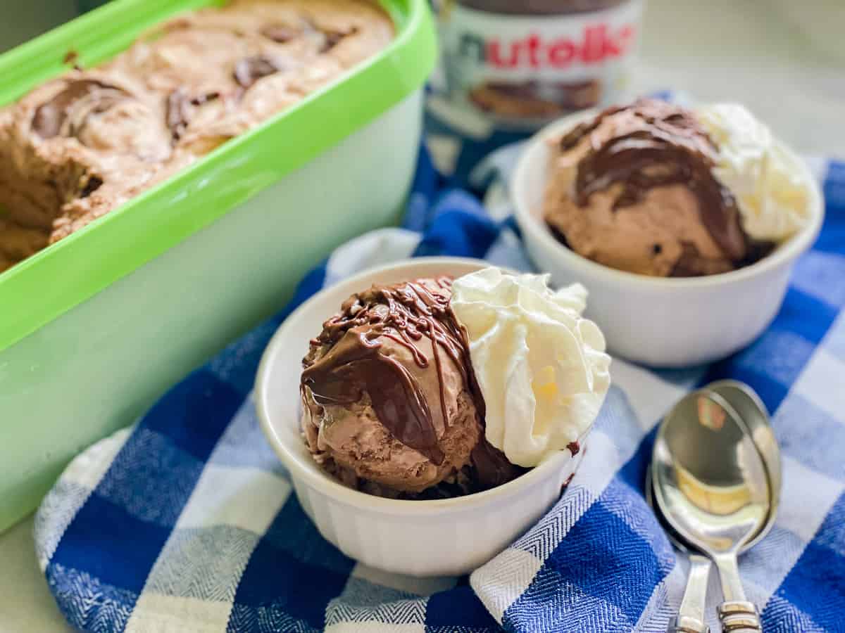 Two white ramekins with chocolaate ice cream, chocolate topping, and whipped cream.