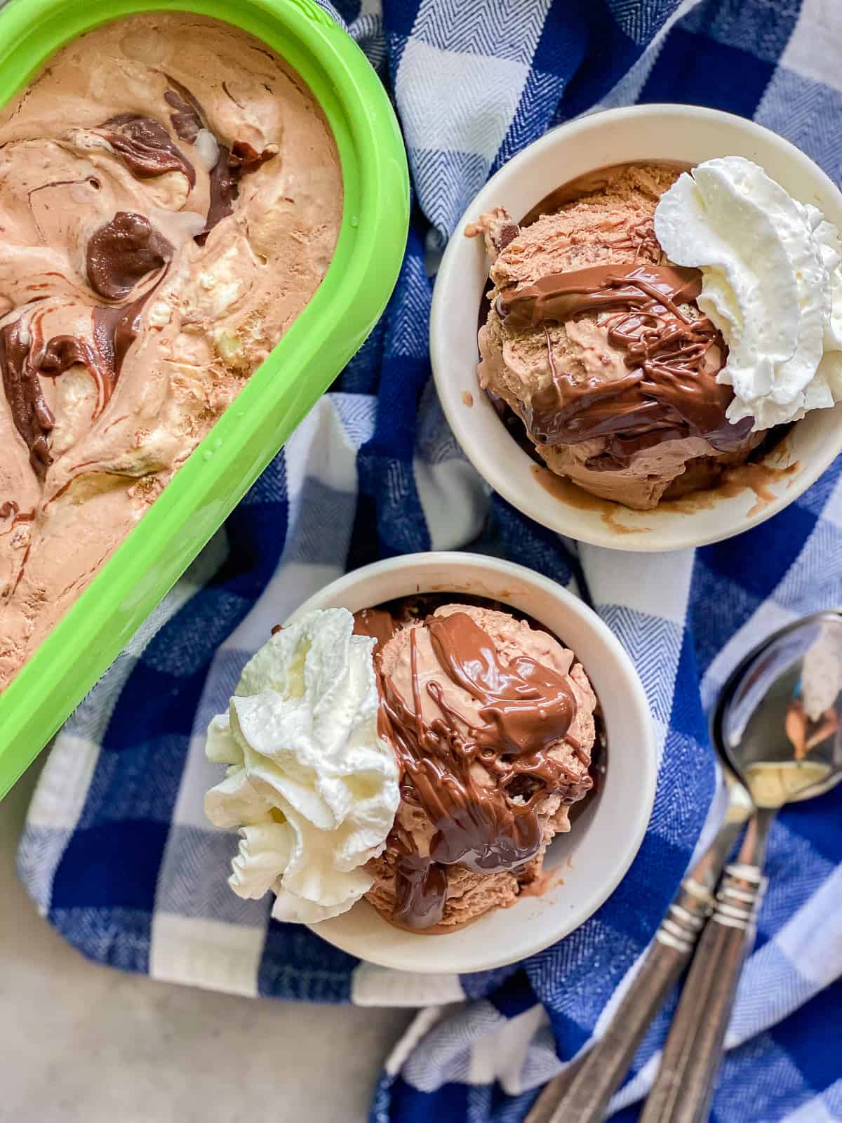 two white ramekins with chocolatae ice cream, chocolate topping and whipped cream.