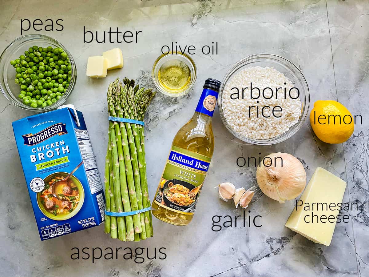 Ingredients on counter; asparagus, arborio rice, butter, oil, onion, garlic, peas, parmesean cheese, broth, lemon, and white wine. 