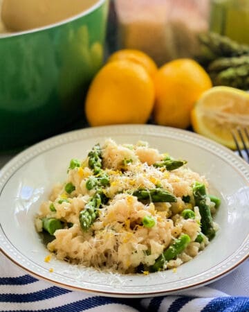 White shallow bowl filled with risotto, asparagus, and peas with grated cheese.