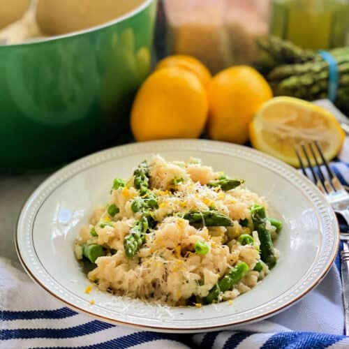 White shallow bowl filled with risotto, asparagus, and peas with grated cheese.
